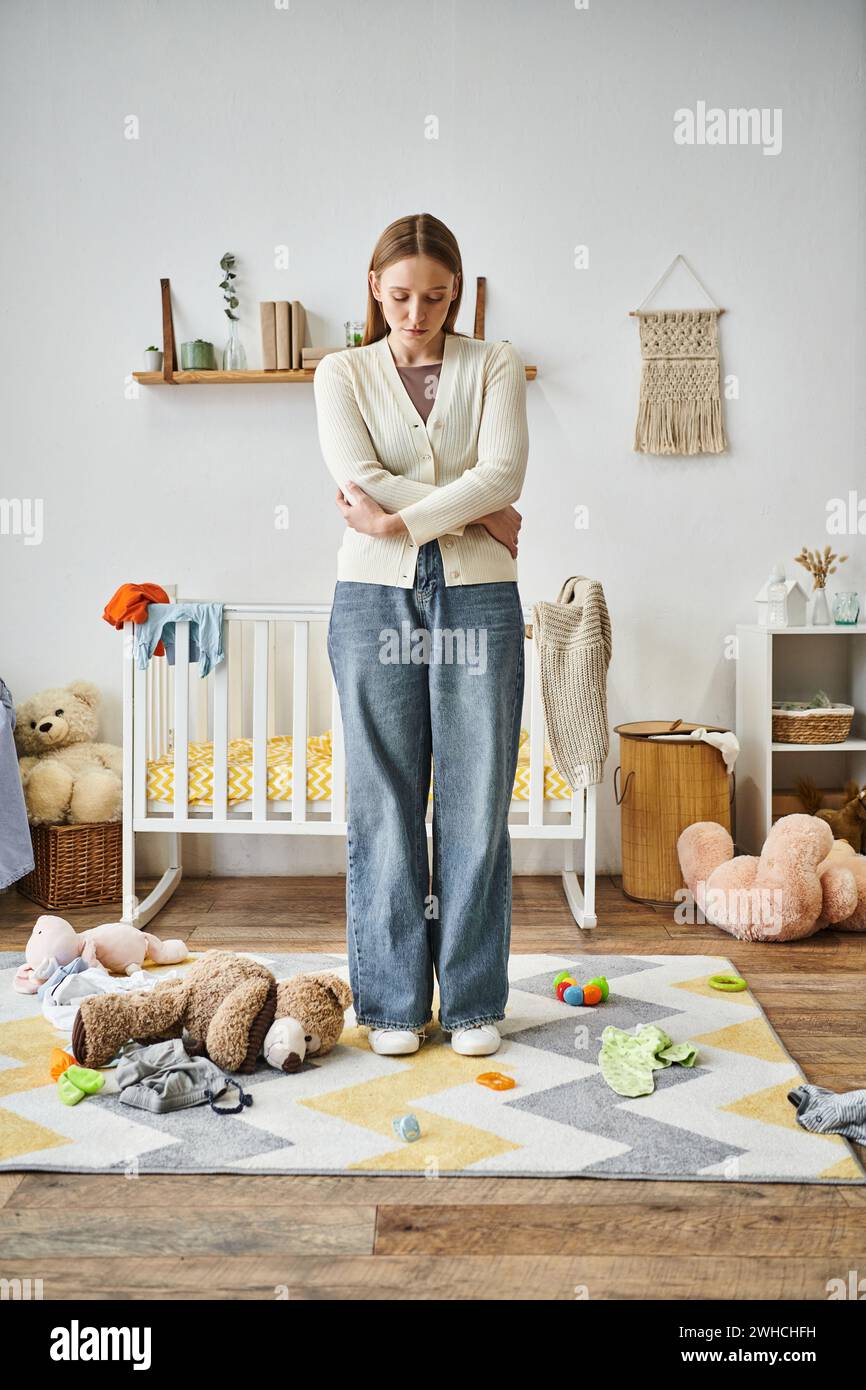 donna esausta e senza speranza con un giocattolo morbido in piedi nella cameretta di casa, momento spezzato Foto Stock