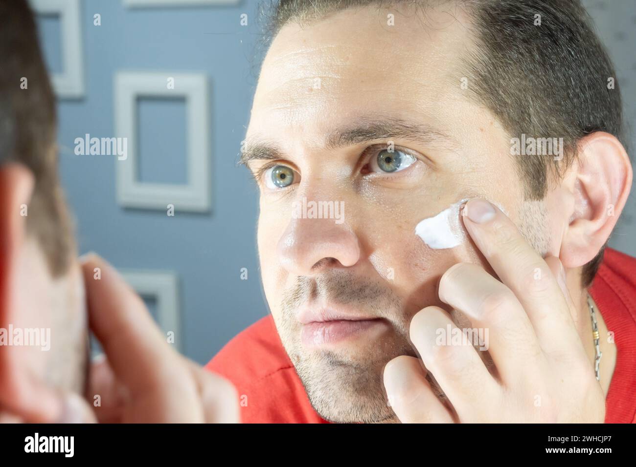 L'uomo applica crema idratante sulla pelle del viso. Cura della pelle degli uomini. Dermatologia e cosmetici da uomo. Foto Stock
