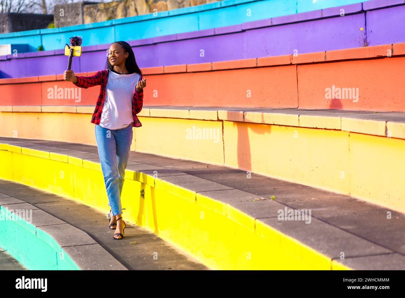 Creazione di contenuti sui social media di giovani donne africane che si registrano in un parco urbano colorato Foto Stock