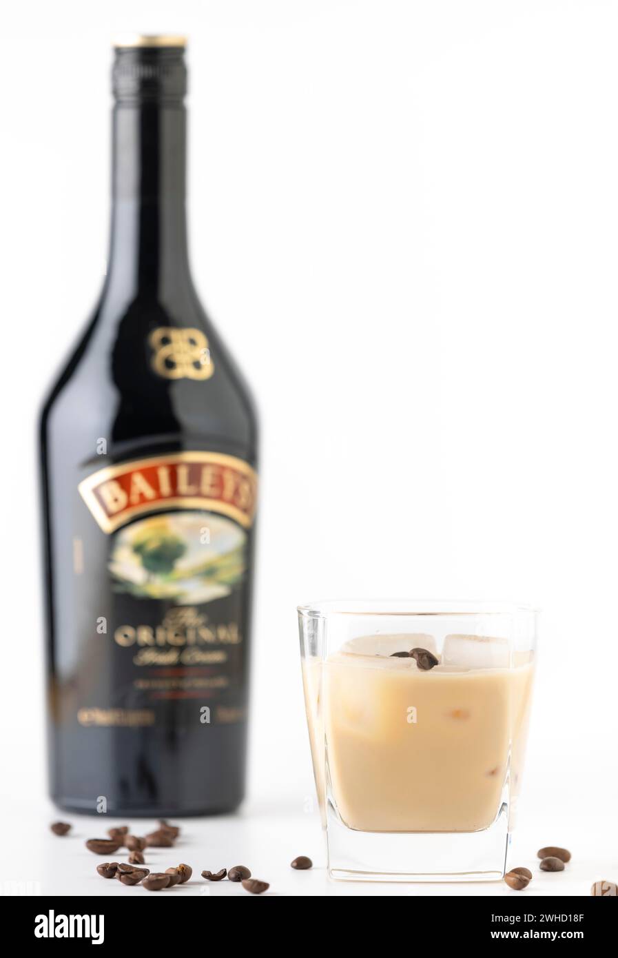Un bicchiere con Bailey e ghiaccio, circondato da chicchi di caffè, una bottiglia sullo sfondo fuori fuoco Foto Stock