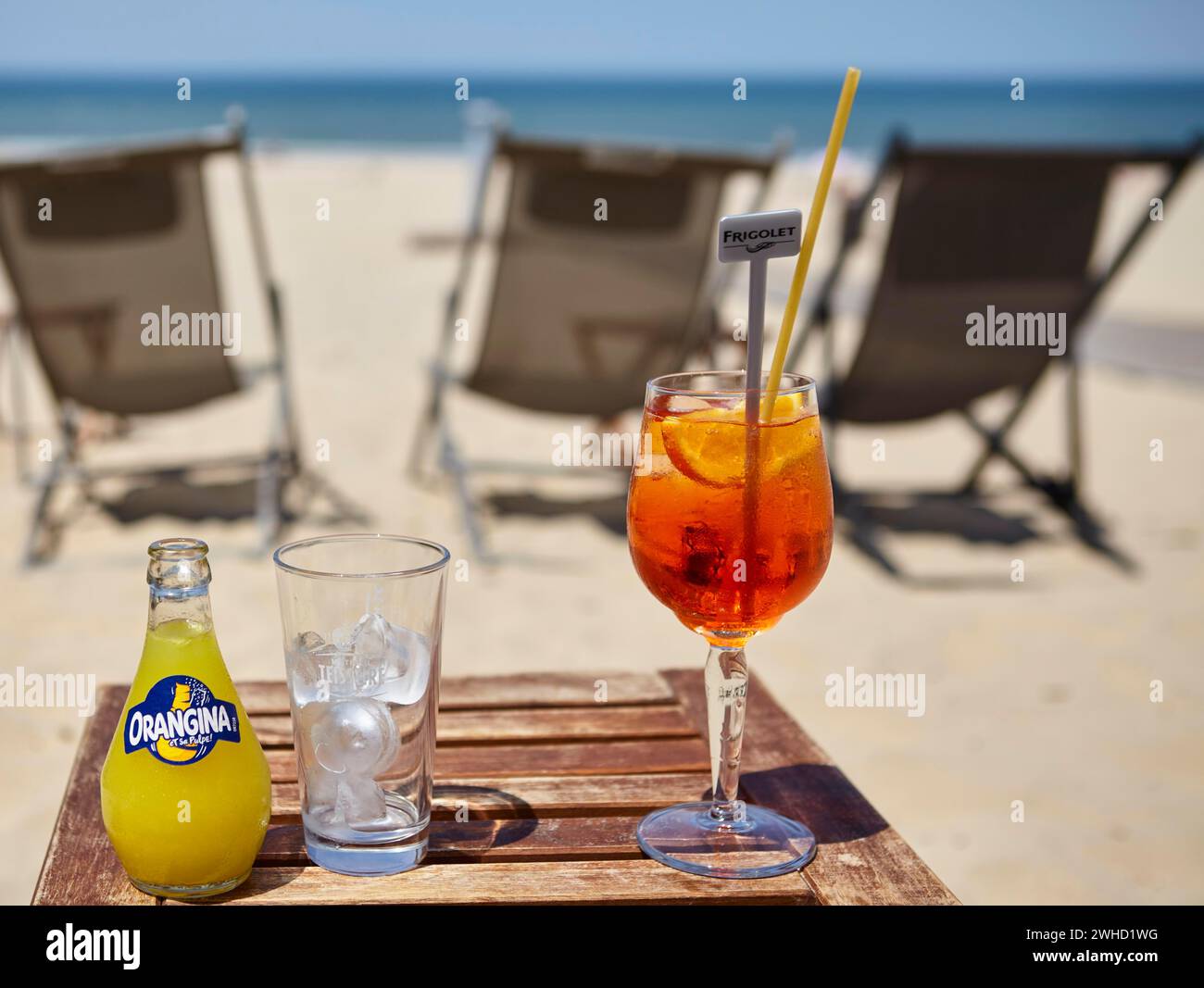 Una bottiglia di Orangina, un bicchiere con cubetti di ghiaccio e un bicchiere di Aperol Spritz con una paglia in un bar sulla spiaggia a Soulac-sur-Mer, Gironde Foto Stock