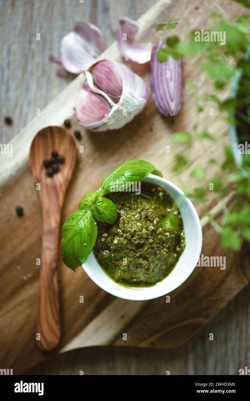 Pesto verde con grani di pepe su un cucchiaio di legno e aglio sullo sfondo, fotografia del cibo Foto Stock