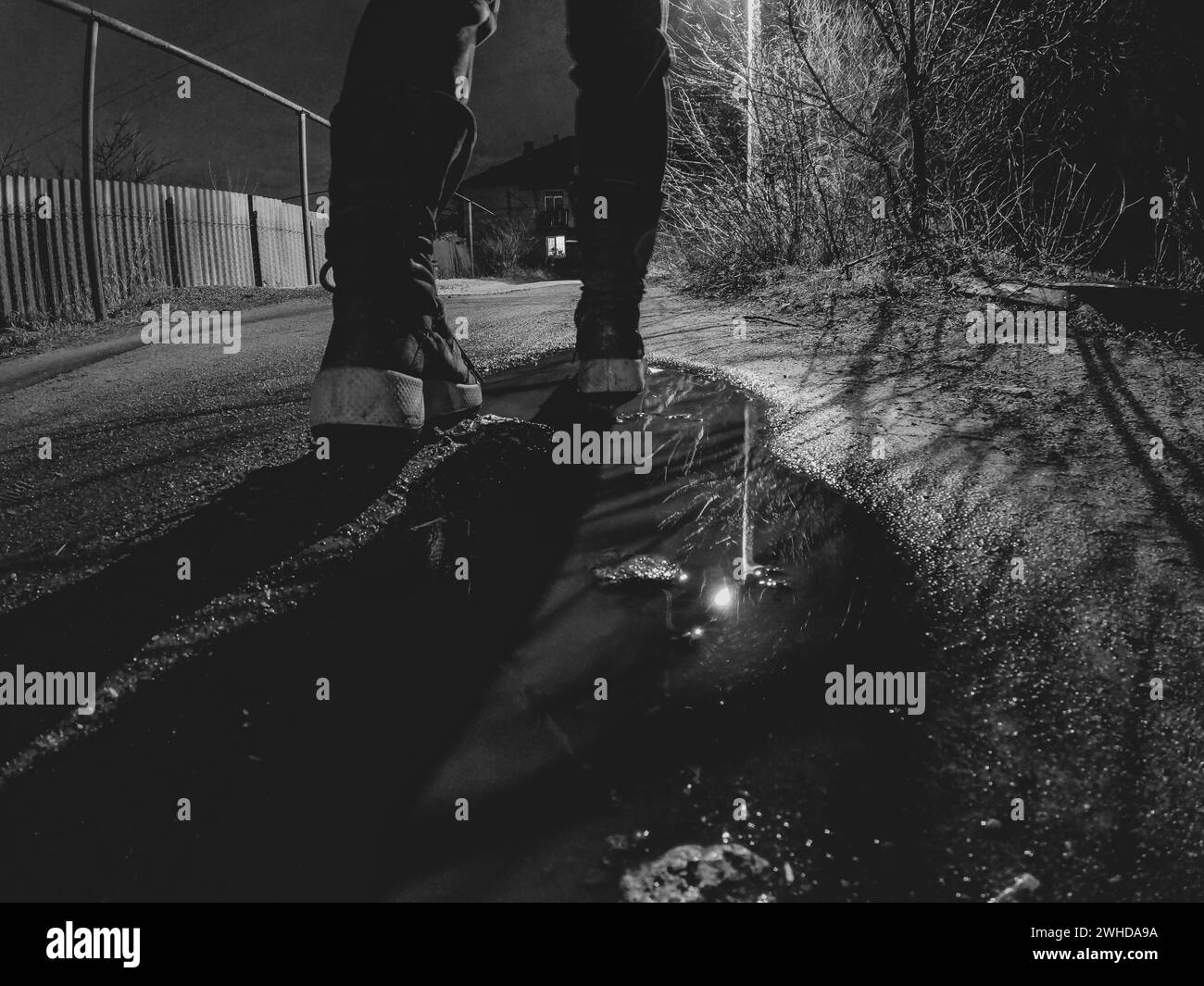 Una ragazza cammina lungo una bagnata strada invernale fino a casa al buio, vista dal basso verso l'alto, foto in bianco e nero, piedi sulla strada al buio Foto Stock