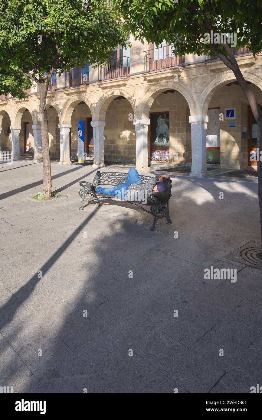 Jerez de la Frontera, Spagna - 3 febbraio 2024: Persona che dorme su una panchina al sole in piazza Arenal a Jerez de la Frontera, Spagna. Foto Stock