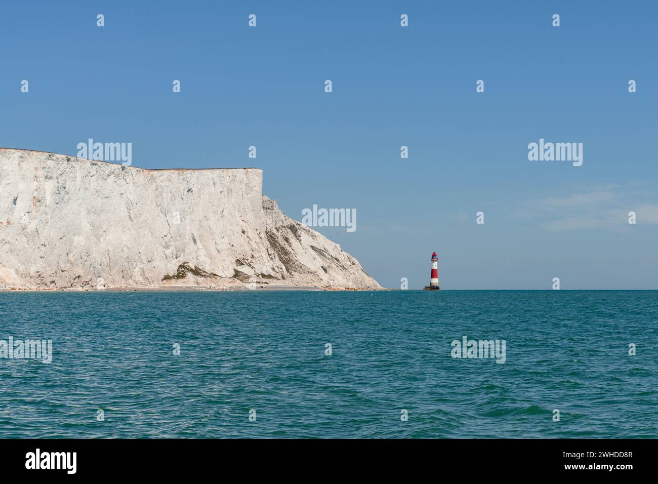 Vista delle scogliere di gesso Beachy Head e Seven Sisters sulla costa dell'Inghilterra meridionale, nel Sussex, un faro si erge di fronte ad esso, nell'acqua, con un cielo blu brillante Foto Stock