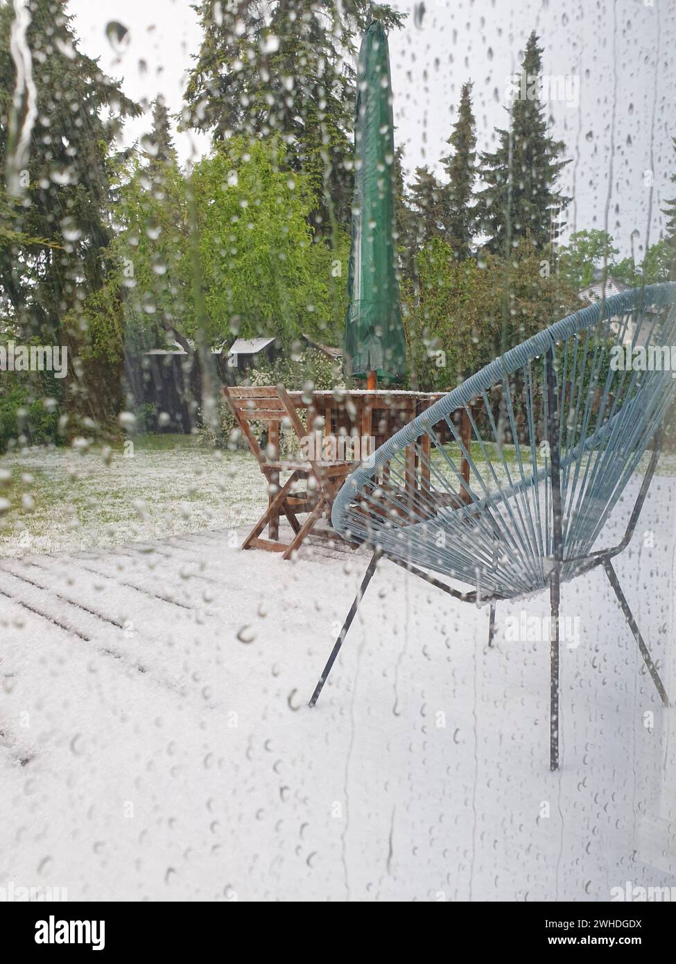 Vista dalle gocce di pioggia sulla finestra delle piante verdi all'esterno e del fenomeno meteorologico della neve a maggio a Berlino a causa dei cambiamenti climatici Foto Stock