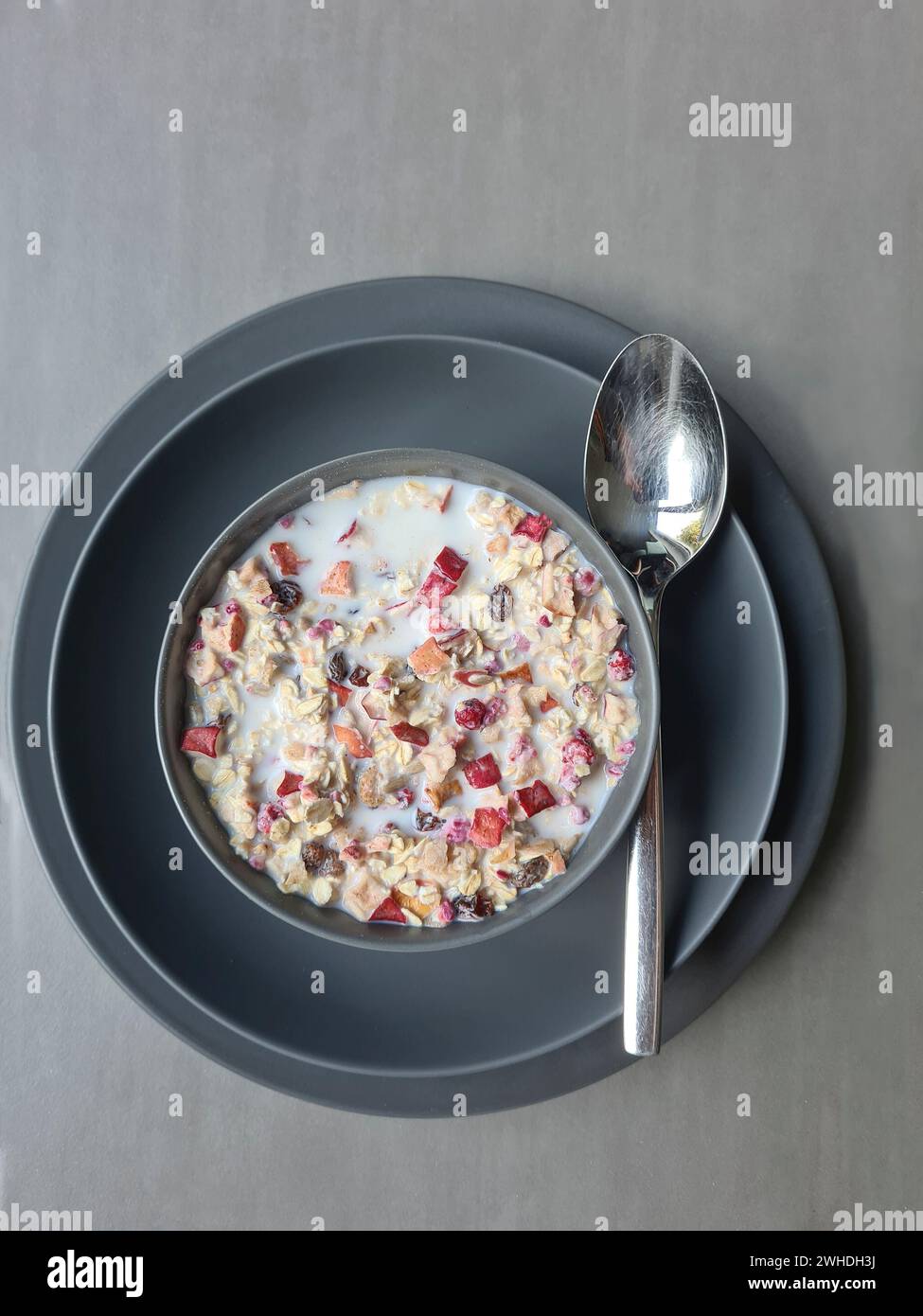Muesli con latte in una ciotola su due piatti grigi con un cucchiaio per colazione, muesli di frutta con cereali e frutta Foto Stock