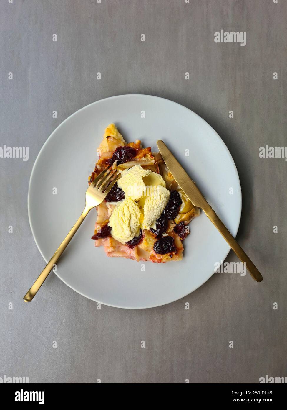 Una fetta di torta di prugne con gelato alla vaniglia servita su un piatto con forchetta e coltello Foto Stock