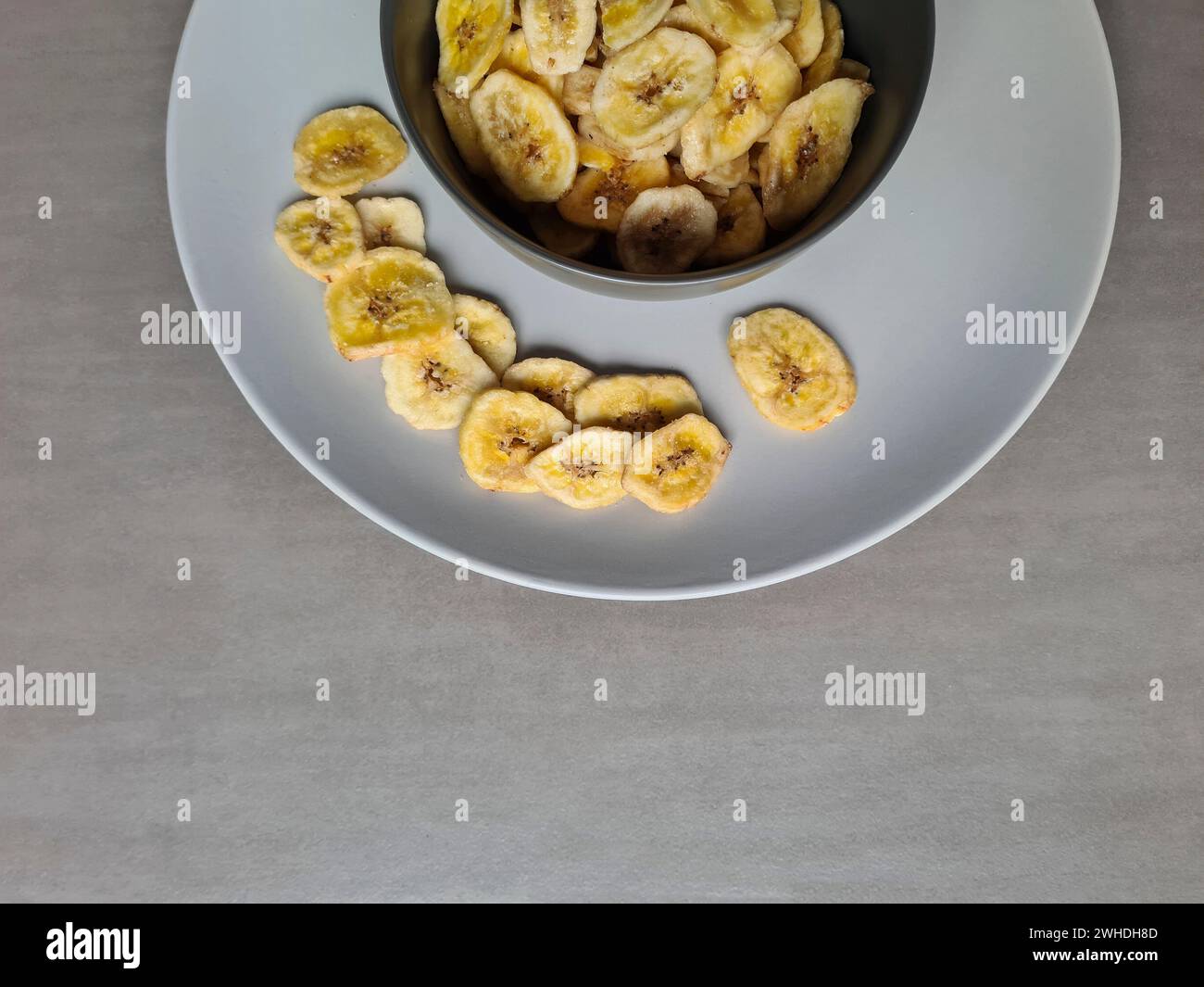 Le patatine di banana in una ciotola grigia su un piatto grigio chiaro come dessert e spuntino tra un pasto e l'altro Foto Stock