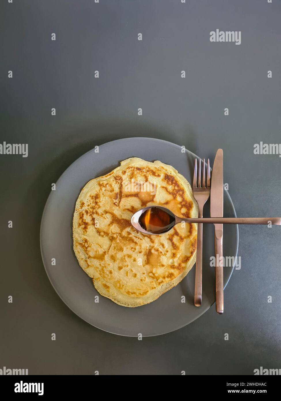 Pancake su piatto grigio con coltello da posate, forchetta e cucchiaio con sciroppo d'acero in rame opaco su sfondo grigio Foto Stock