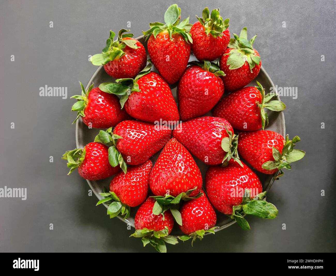 Fragole rosse fresche in un recipiente su sfondo grigio Foto Stock