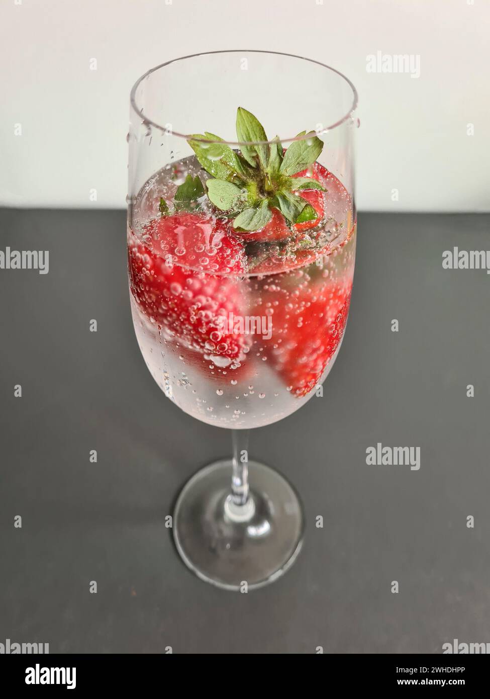 Fragole fresche rosse intere mature con acqua minerale in un bicchiere di champagne come bevanda rinfrescante analcolica in estate Foto Stock