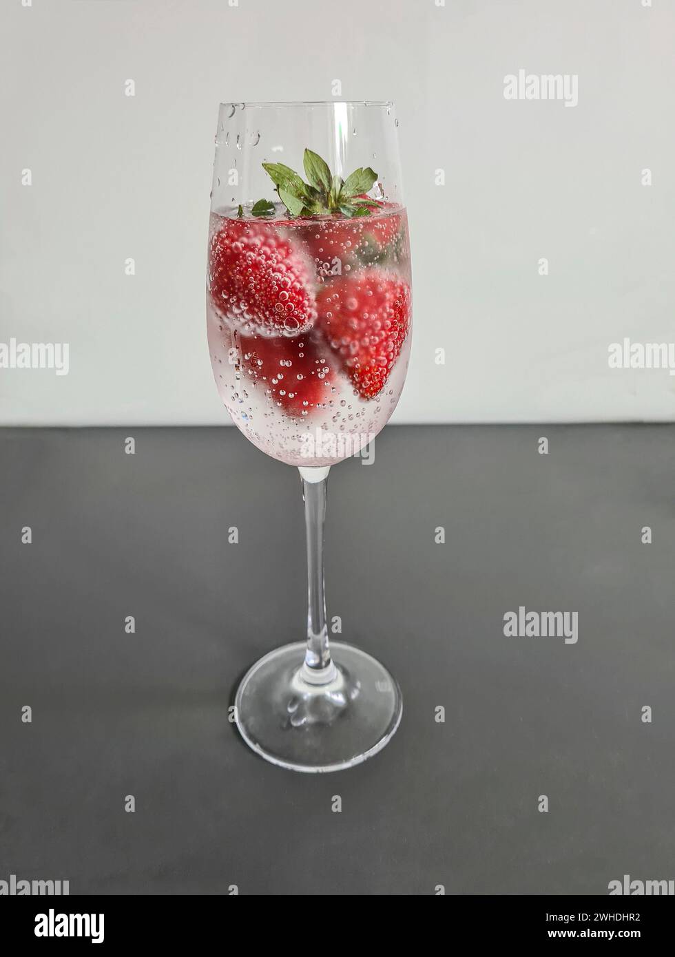 Fragole fresche rosse intere mature con acqua minerale in un bicchiere di champagne come bevanda rinfrescante analcolica in estate Foto Stock