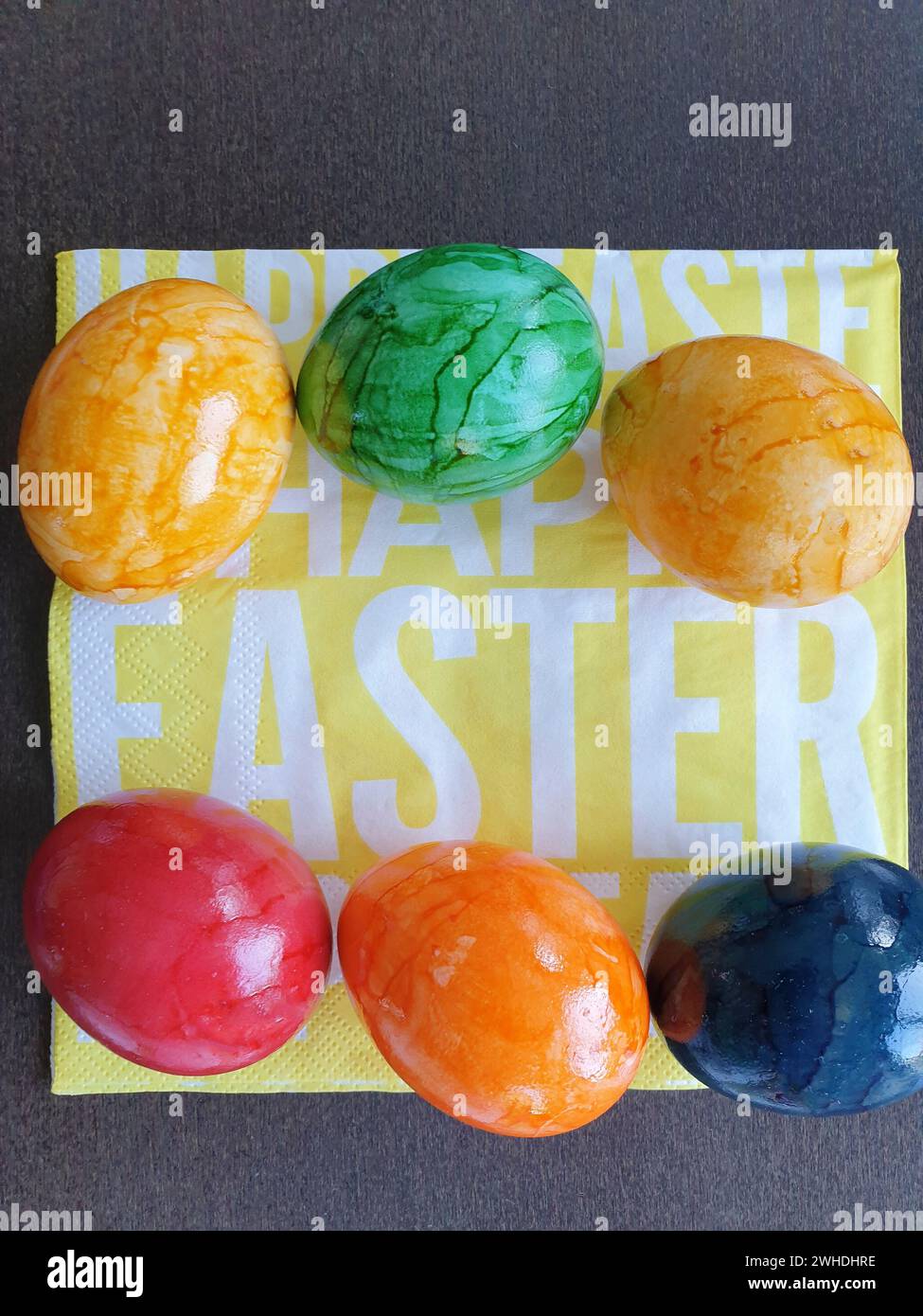 Uova bollite colorate nei colori giallo verde blu e rosso giacciono su un tovagliolo giallo con scritta bianca per Pasqua Foto Stock