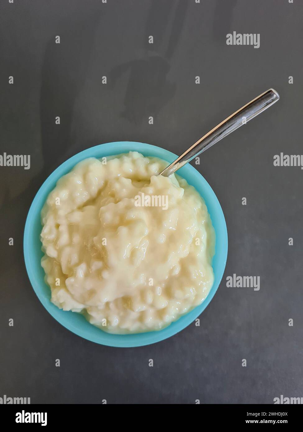 Budino di riso con cucchiaio in una ciotola di vetro su sfondo grigio alla luce del giorno Foto Stock