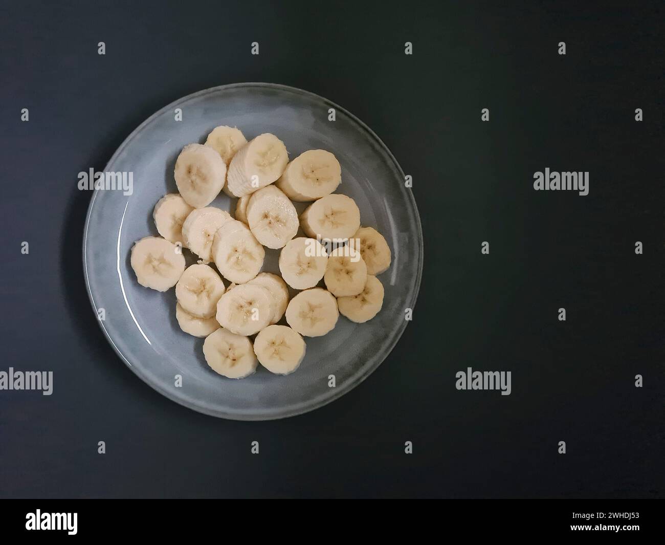 Fette di banana tagliate su un piatto blu chiaro come dessert sano su uno sfondo scuro Foto Stock
