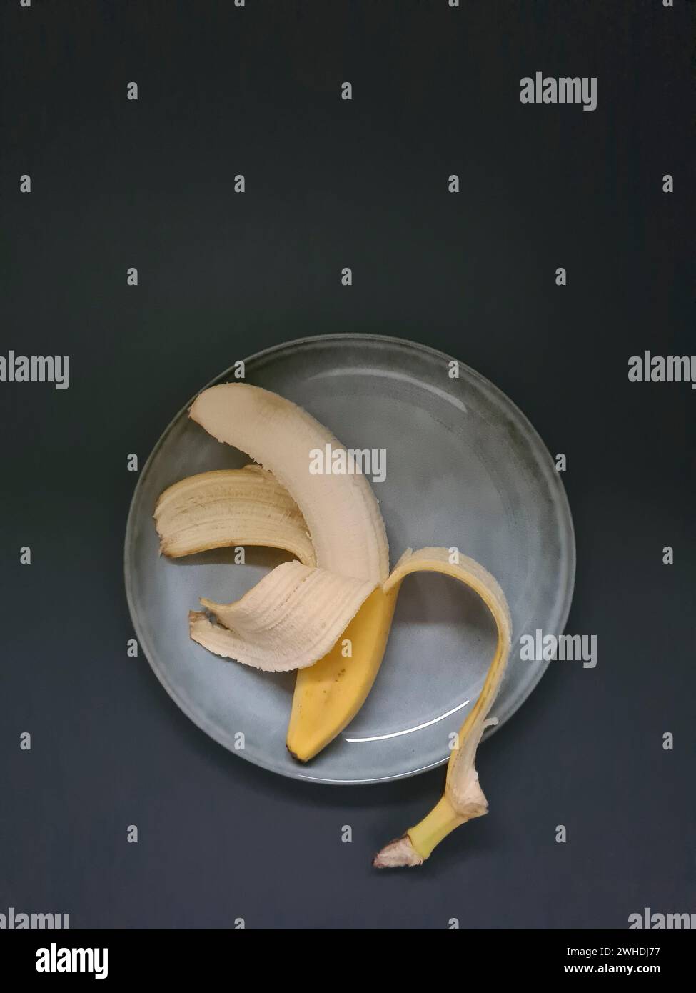 banana gialla sbucciata a metà su un piatto azzurro Foto Stock