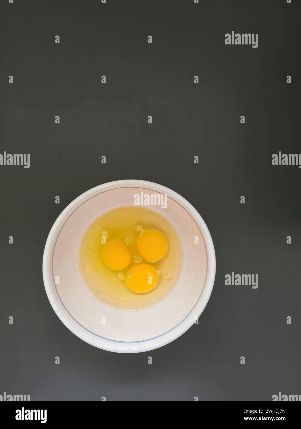 Tre uova crude sbattute, albumi e tuorli in un recipiente bianco Foto Stock