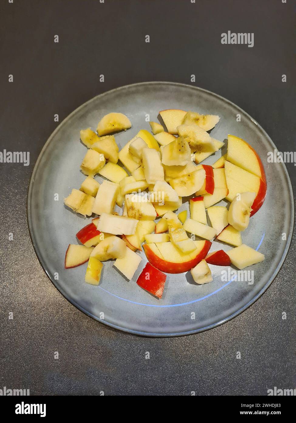 Pezzi di mela con buccia di mela rossa tagliati a pezzetti come Macedonia di frutta su un piatto azzurro Foto Stock