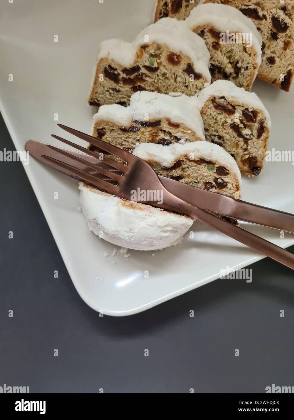 Primo piano di diverse fette di stollen natalizio su un piatto di porcellana bianca con coltello e forchetta Foto Stock