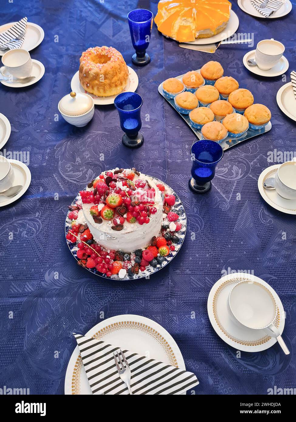 Un tavolo di compleanno decorato a festa con varie torte e pasticcini su una tovaglia blu Foto Stock