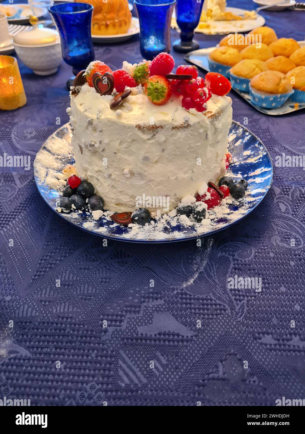 Una torta alla panna natalizia con frutta come fragole, lamponi, ribes e mirtilli come decorazione si staglia su una tovaglia blu Foto Stock
