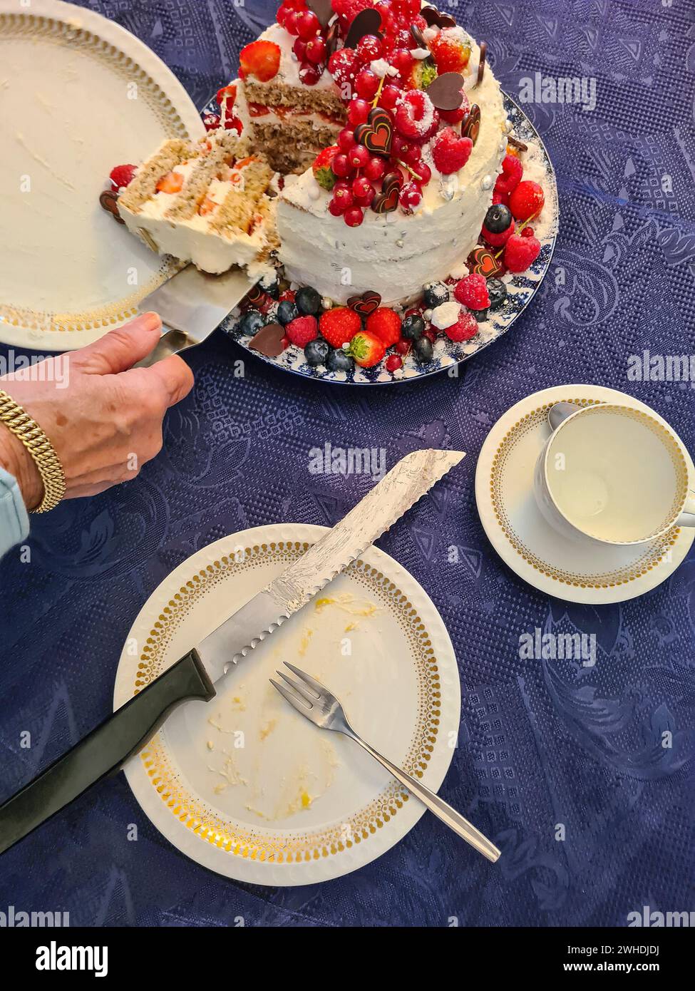 La mano di una signora anziana prende un pezzo della torta e lo solleva su un piatto con un cameriere Foto Stock