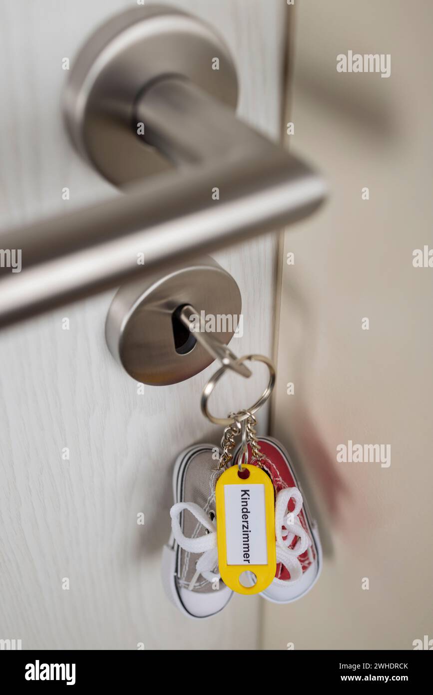 Chiave con portachiavi giallo e scarpe da ginnastica in miniatura bloccate nella serratura della porta, con etichetta ëKinderzimmerë, Foto Stock