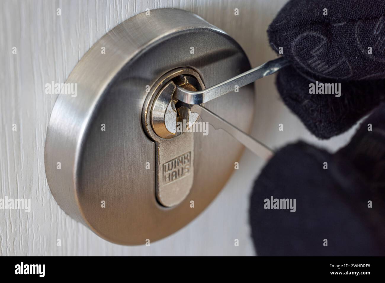 Il ladro apre la serratura a cilindro con lo strumento per il prelievo a blocchi, la mano dell'uomo con il guanto, dettaglio, immagine simbolica, furto, Foto Stock