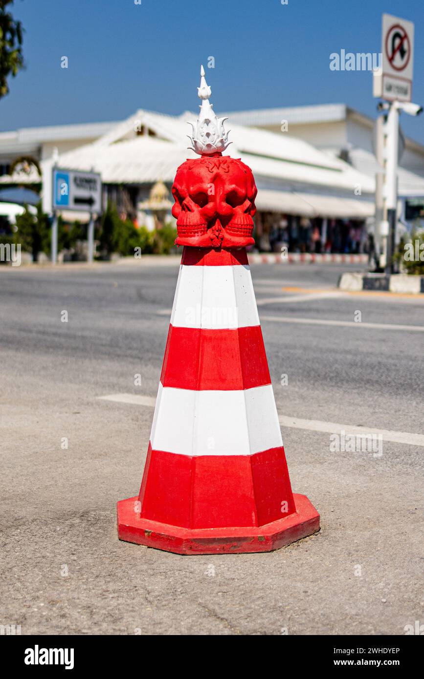 Un pilone arancione e bianco con un teschio scolpito in cima al Tempio bianco di Chiang Rai Foto Stock