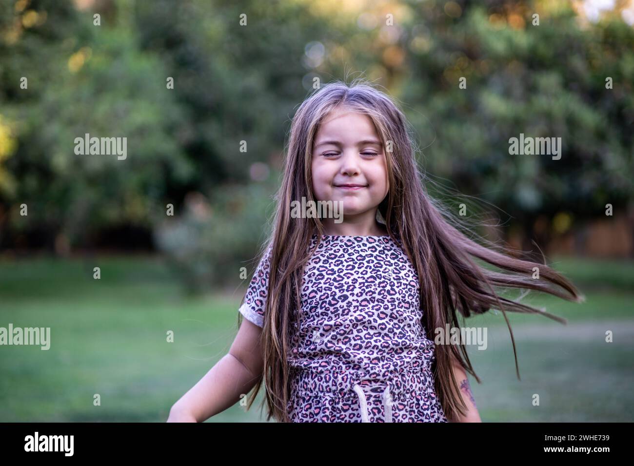 Hermosa muchacha rubia con gracia mientras disfruta de la naturaleza en un escenario al aire libre lleno de verdor y luz y recostada en el césped Foto Stock