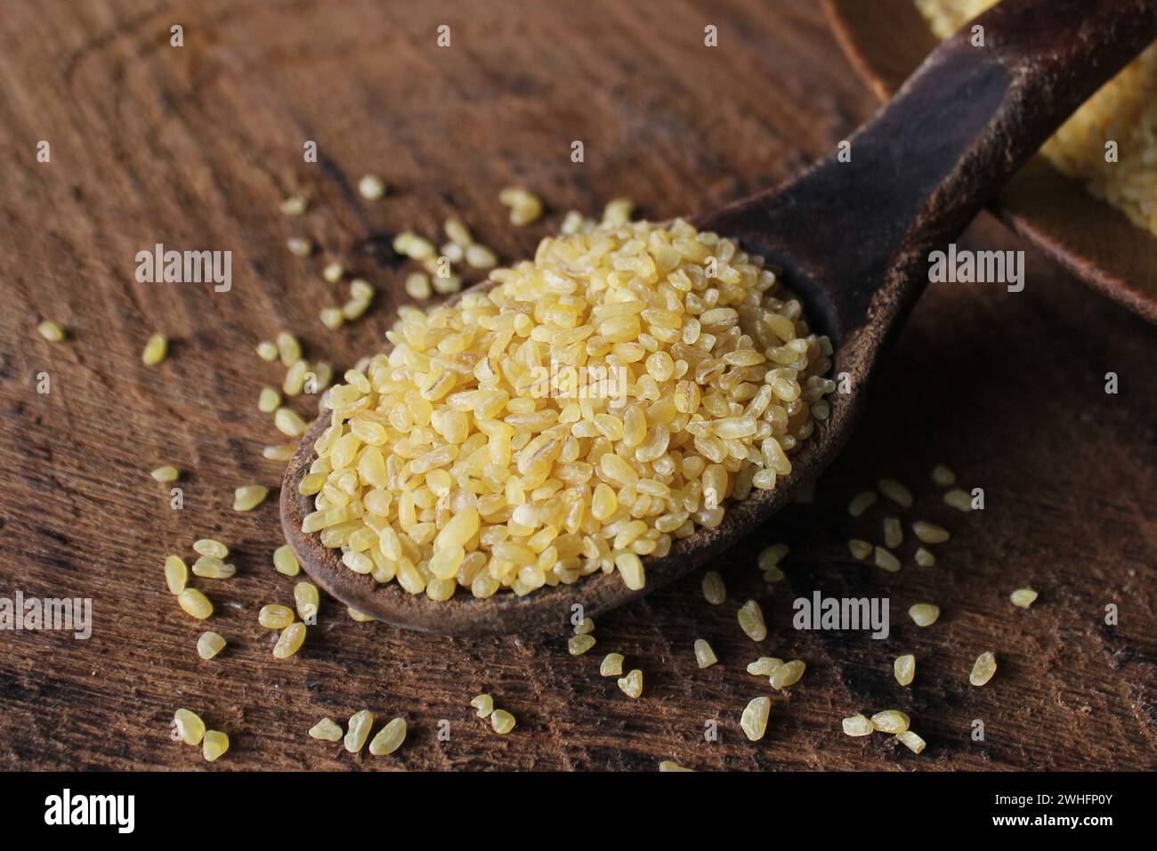 Grano bulgaro secco in cucchiaio di legno isolato bulgur versato Foto Stock