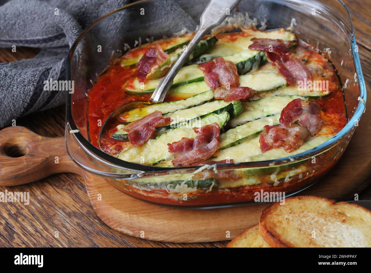 Padella con pomodori fritti, zucchine, il formaggio e le erbe sul tagliere di legno Foto Stock