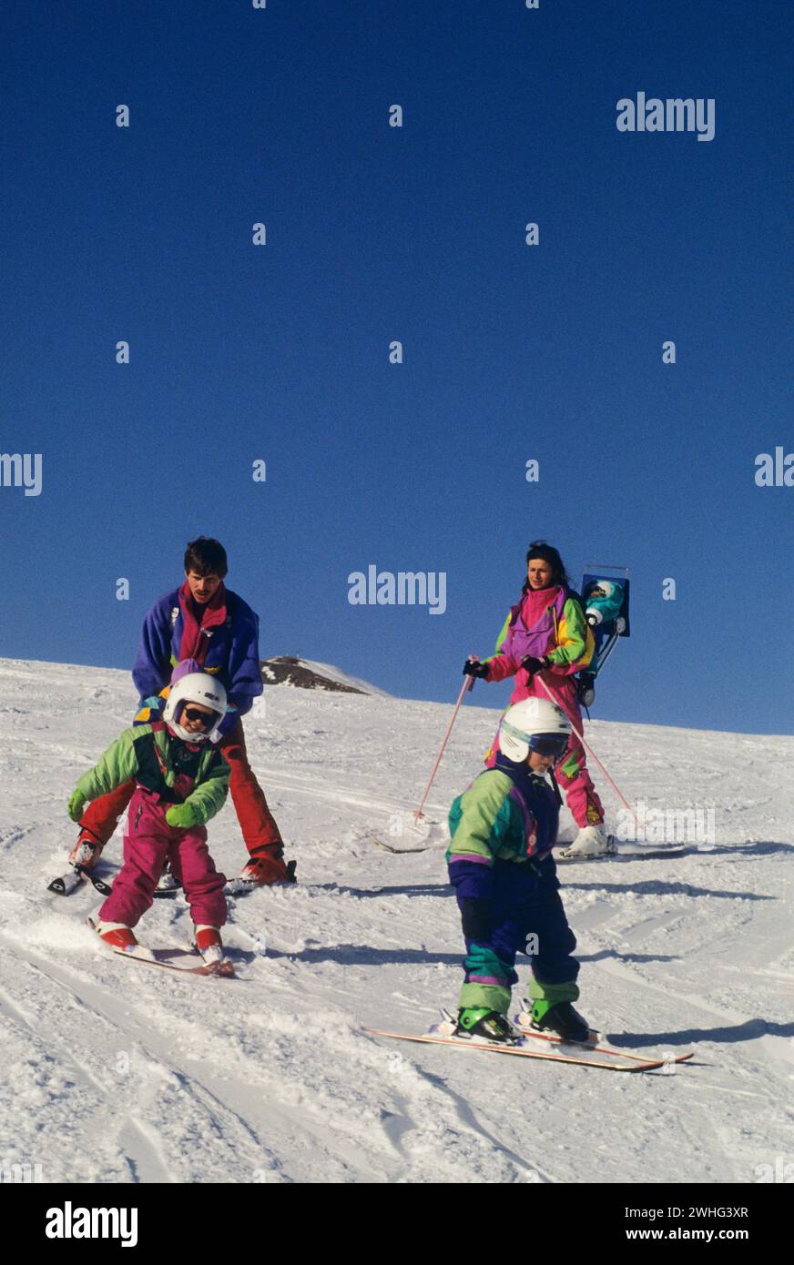 famiglia pattinaggio con 3 bambini cielo azzurro sfondo vacanze invernali vacanze vacanze ski famille tenue colorees joie de vivre ski alpin Foto Stock