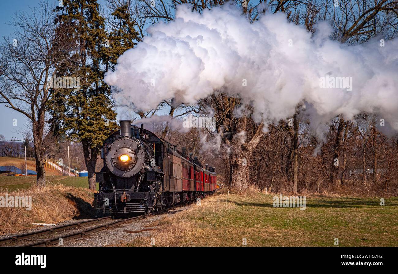 Antico treno passeggeri a vapore in avvicinamento su un singolo binario che soffia fumo Foto Stock
