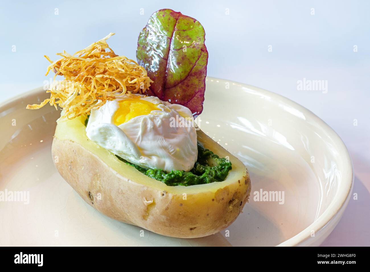 Uova in camicia, spinaci e paglia di sedano fritta ripiena in una barca di patate cotta e una foglia di erbe selvatiche a vela, piatto creativo su una liga Foto Stock