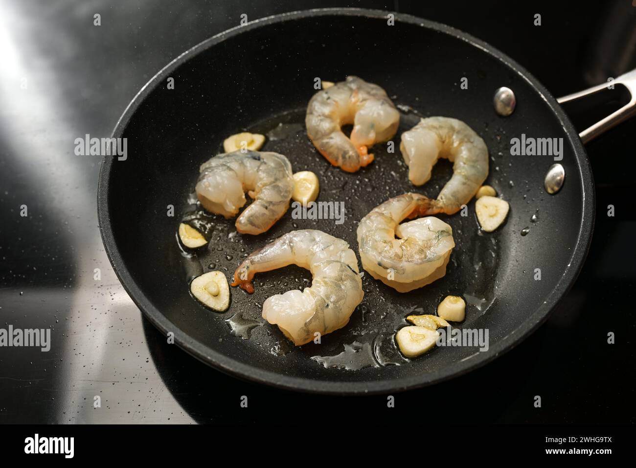I gamberetti pelati crudi e l'aglio vengono saltati in una pentola sul piano cottura nero, preparati per un delizioso antipasto, copia spazio Foto Stock