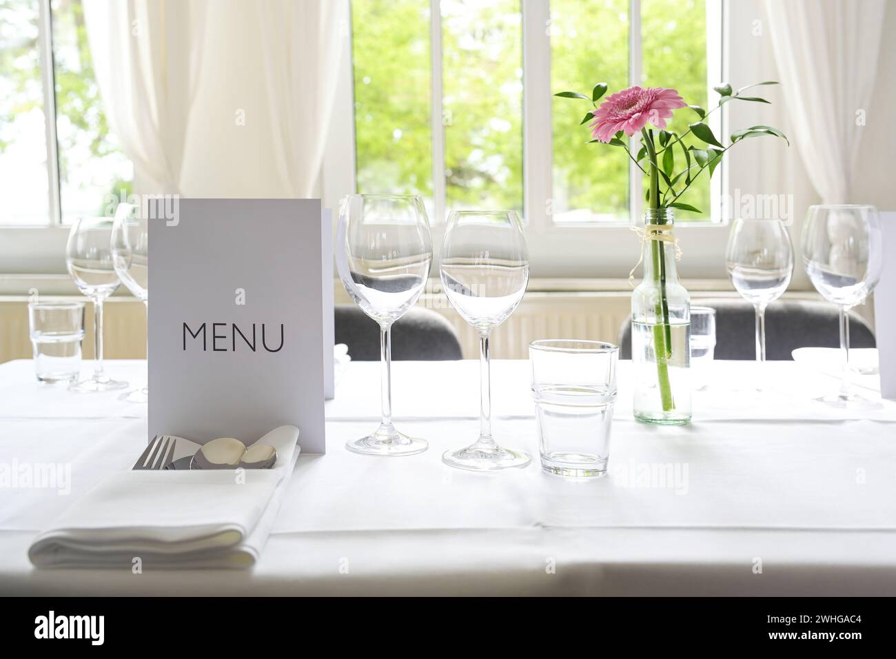 Elegante ambiente da tavola, posto con menu a carte, bicchieri, posate, tovagliolo e un fiore rosa su una tovaglia bianca per una cena festosa Foto Stock