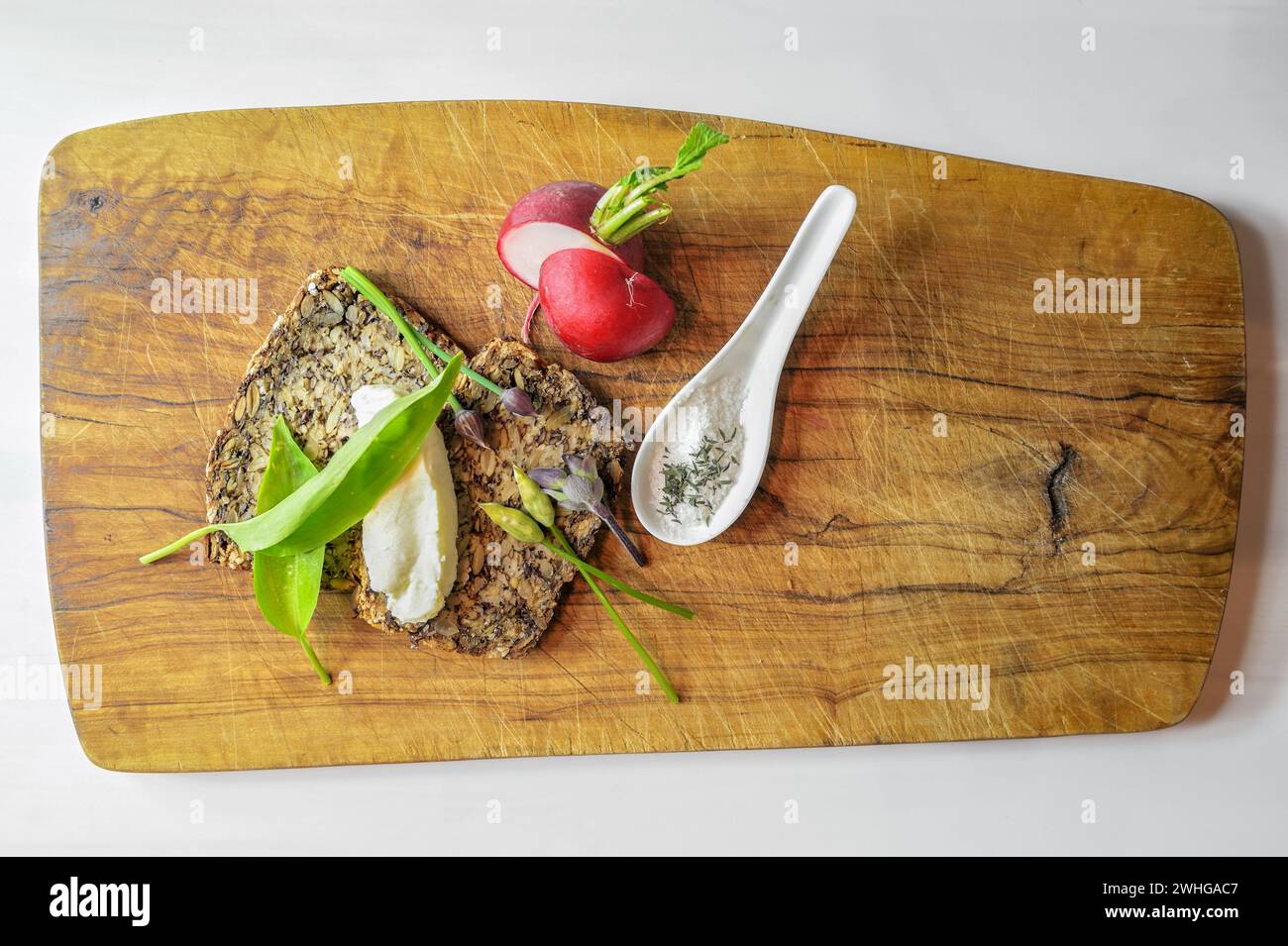 Pane integrale con burro, ravanello, un cucchiaio di sale e aglio selvatico su una tavola rustica di legno, sano pasto naturale, semplice Foto Stock