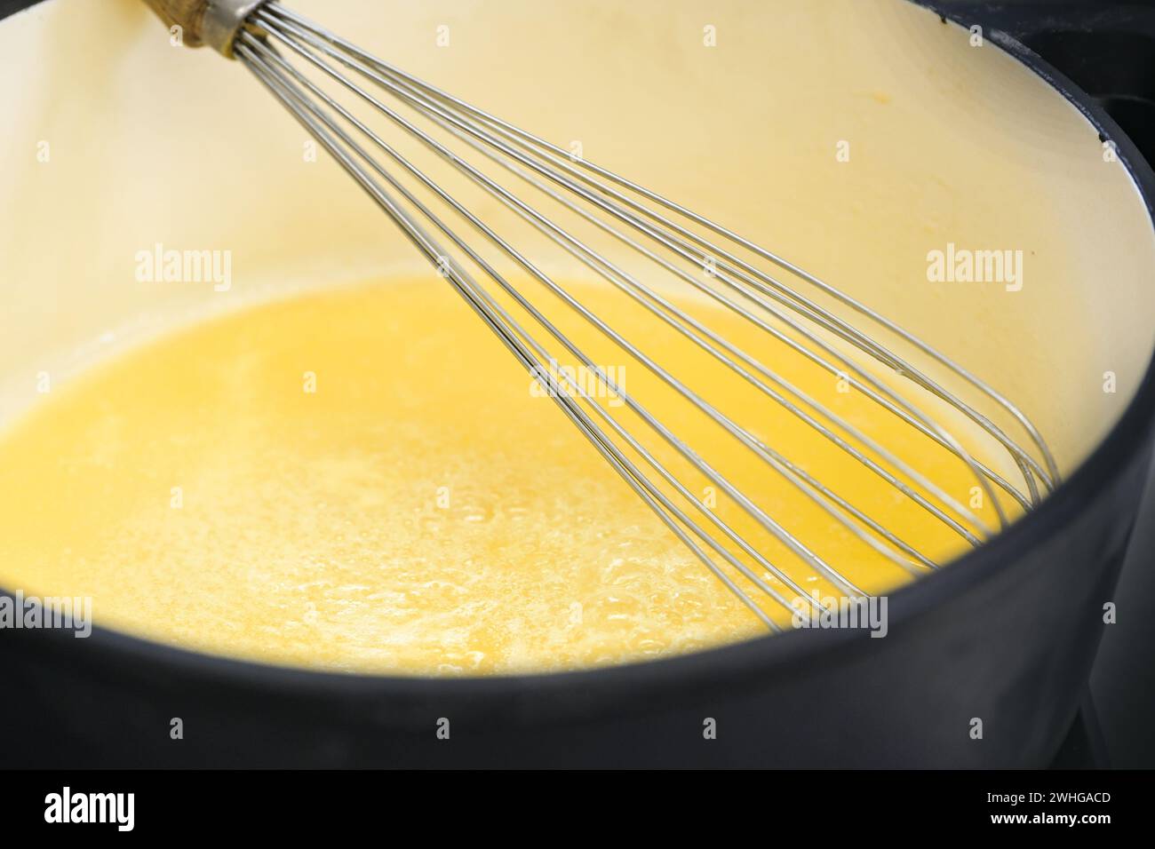 Frusta con filo metallico in una pentola con salsa di semola gialla dorata o budino, cuocere un delizioso dessert, copiare spazio, focalizzazione selezionata Foto Stock