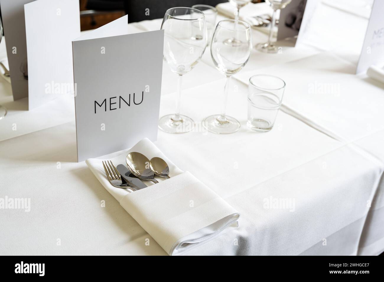 Ambiente elegante con menu a carte, vari bicchieri, posate e tovagliolo su un tavolo con tovaglia bianca per una cena di gala, Foto Stock