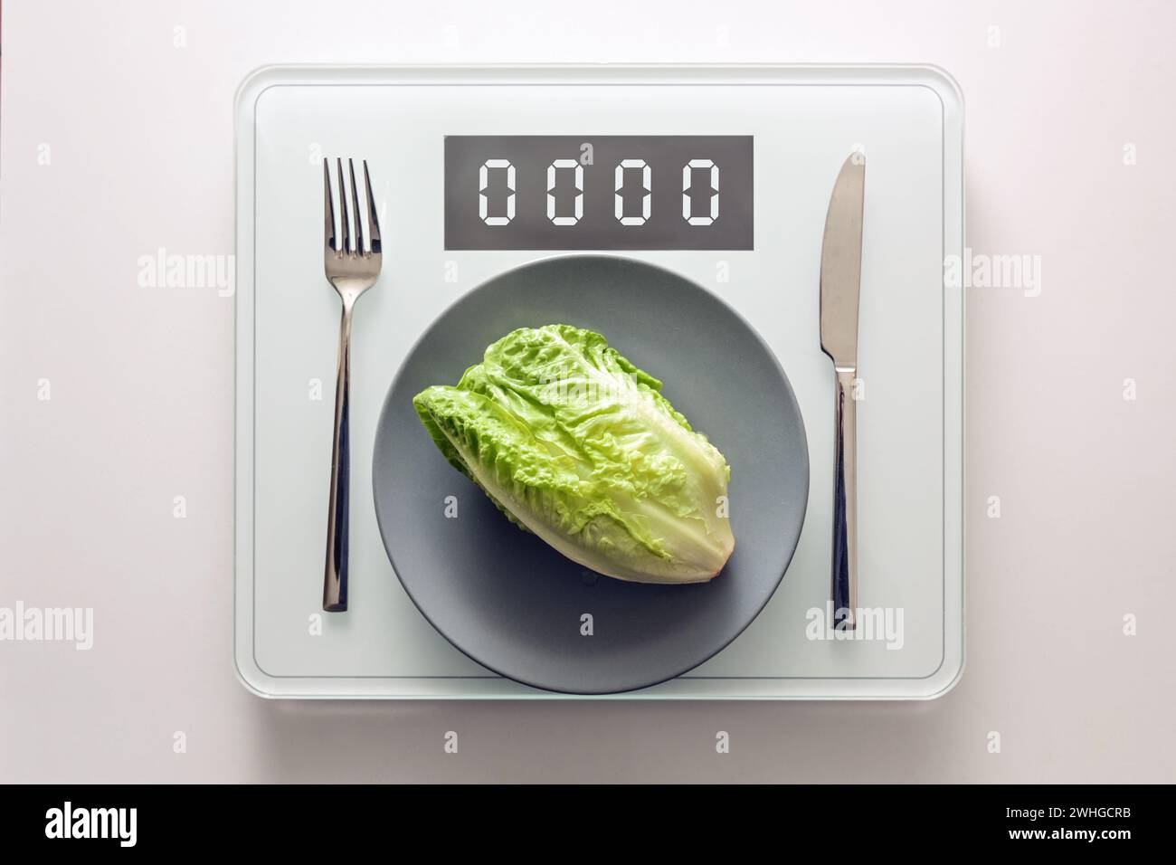 Lattuga verde fresca o baby cos su un piatto grigio e posate su una bilancia digitale che mostra zero, dieta sana e perdere peso Foto Stock