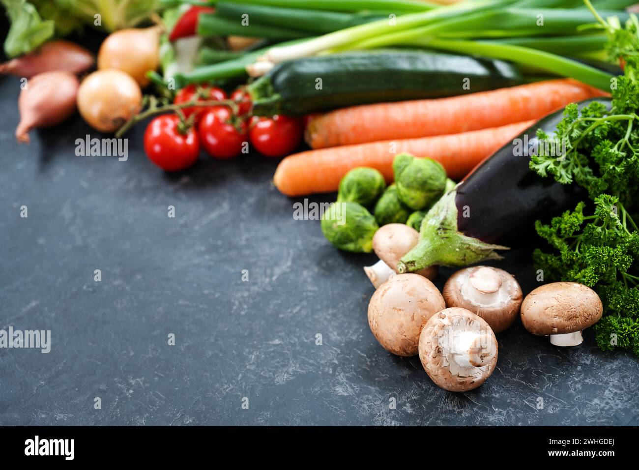 Verdure fresche come funghi, melanzane, carote e molto altro su una superficie di ardesia grigia scura, cibo vegetariano sano per il fitness o. Foto Stock