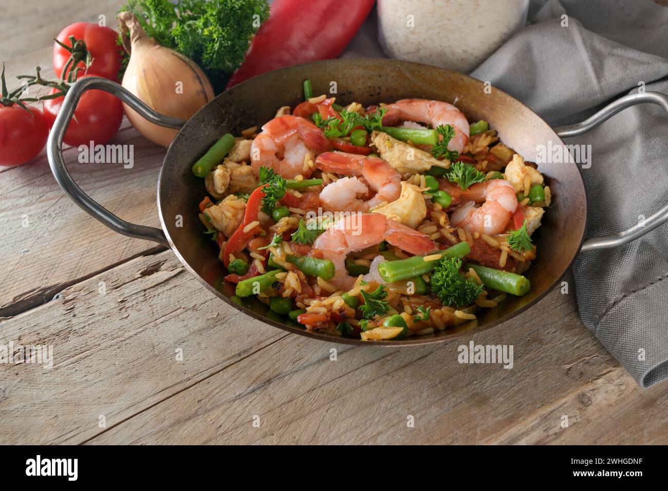 Paella spagnola, piatto di riso con gamberetti, pollo e verdure in una padella piatta su un rustico tavolo in legno, spazio per copiare, focalizzazione selezionata Foto Stock