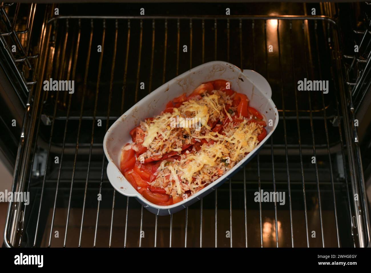 Casseruola con peperoni cotti al forno con riso, tonno, pomodori e formaggio su una griglia nel forno, copia spazio Foto Stock