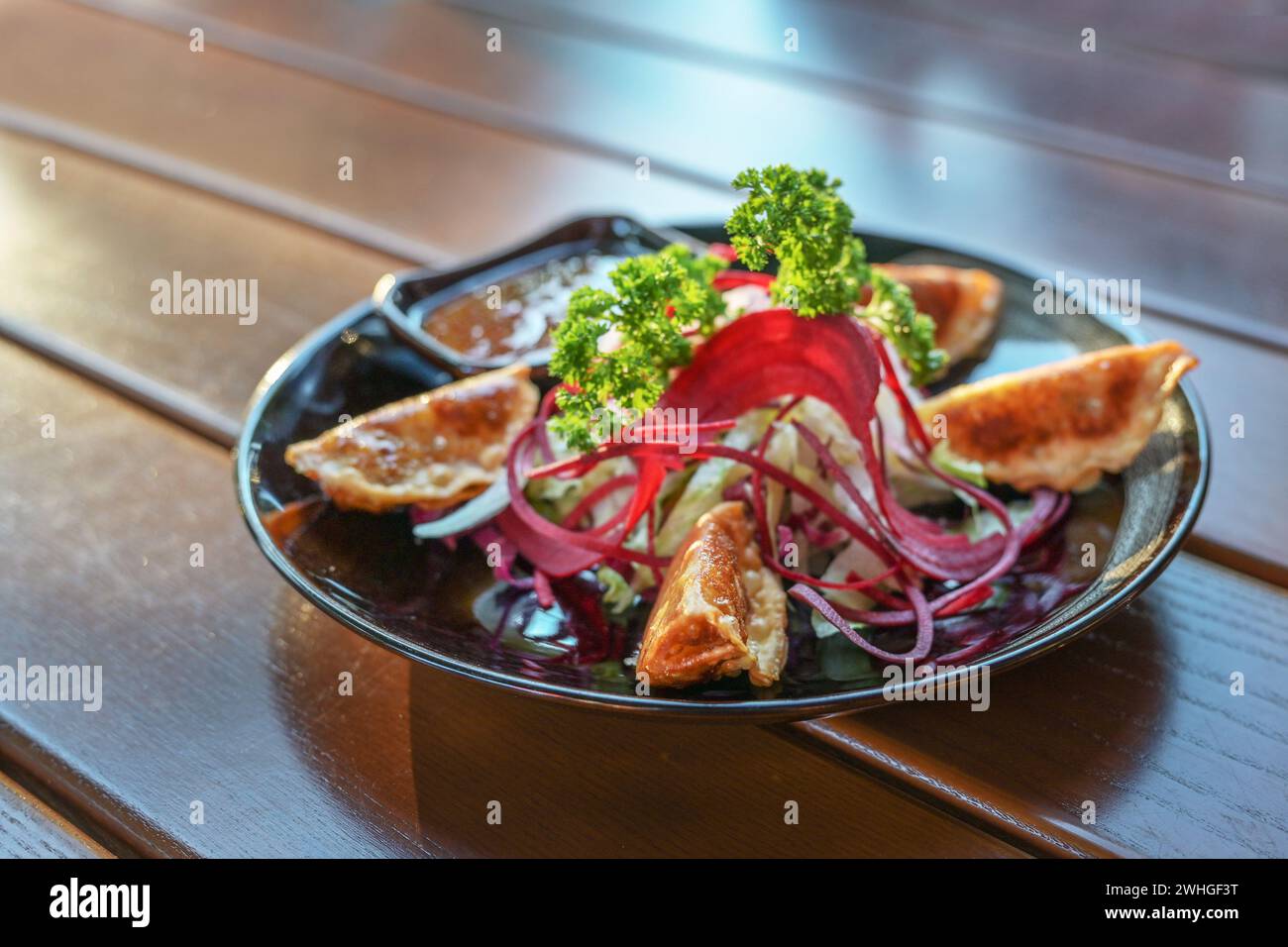 Gyoza fritta in profondità con insalata e salsa servita come antipasto su un piatto nero, piatto asiatico su un tavolo di legno, spazio copia, f Foto Stock
