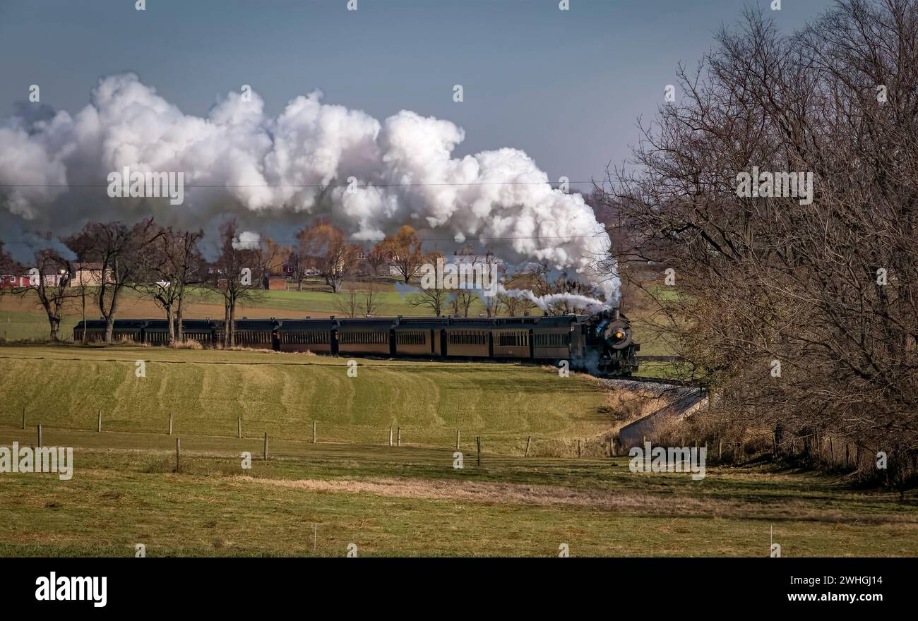 Vista di un antico treno passeggeri che si avvicina, soffia fumo e vapore, in un giorno d'autunno Foto Stock