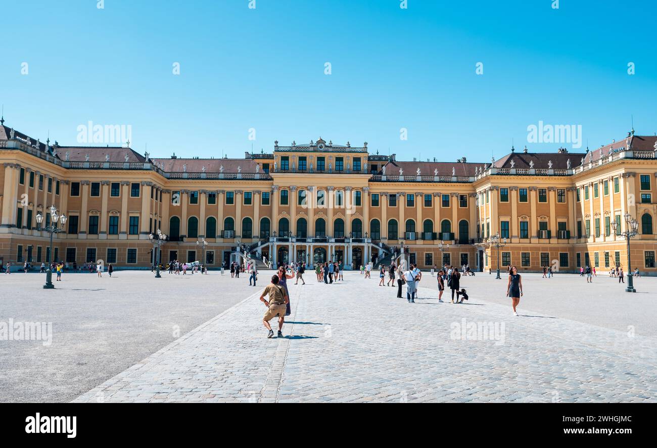 Vienna, Austria - 12 agosto 2022: Il palazzo Schönbrunn di Vienna si erge su una vivace piazza della città mentre la gente si riunisce sotto il cielo estivo, ammirando il gr Foto Stock