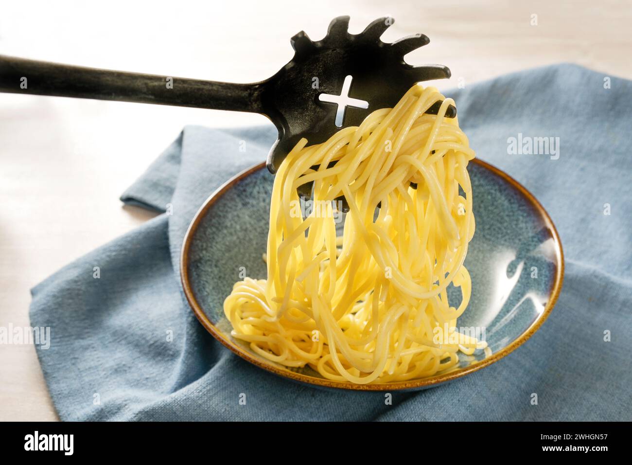 Serve pasta fresca, gli spaghetti vengono ripieni su un piatto blu con un cucchiaio speciale, un tovagliolo su un tavolo leggero, uno spazio per le copie, selezionati Foto Stock