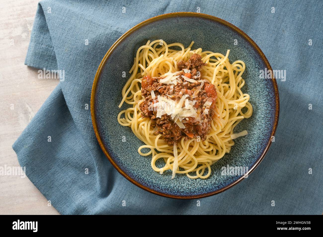 Spaghetti con salsa bolognese di carne macinata e pomodori, guarniti con parmigiano su un piatto blu e tovagliolo, stile italiano Foto Stock